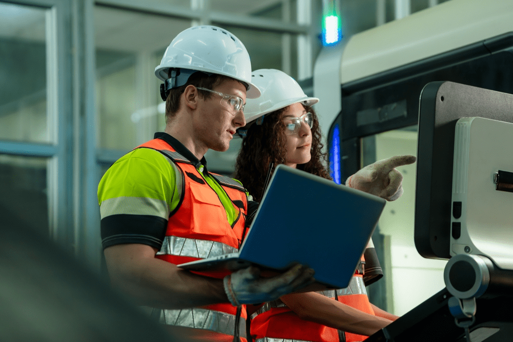 Two workers wearing hard hat is looking into a computer screen